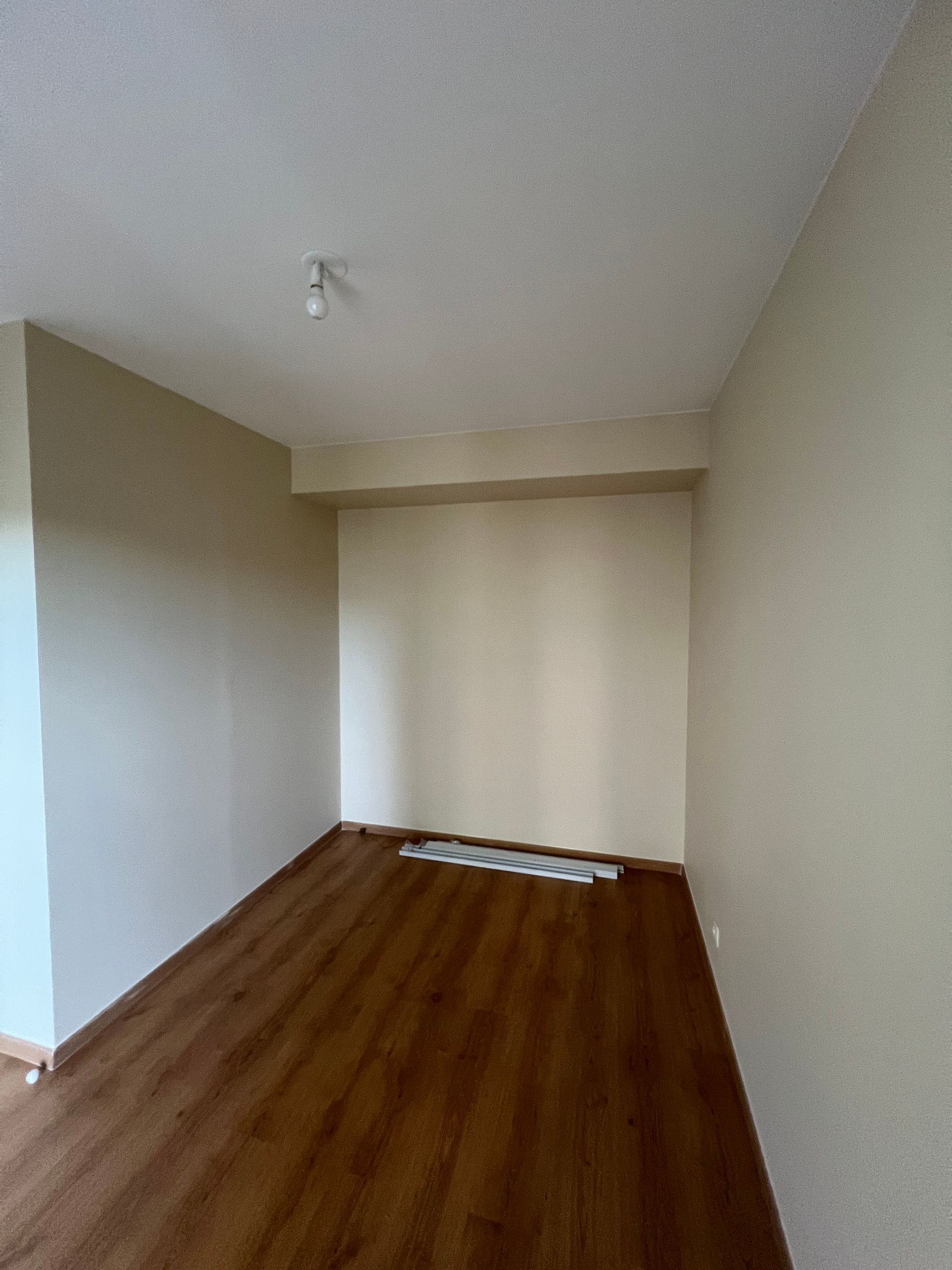 Pièce vide avec parquet, murs beiges et un luminaire au plafond.