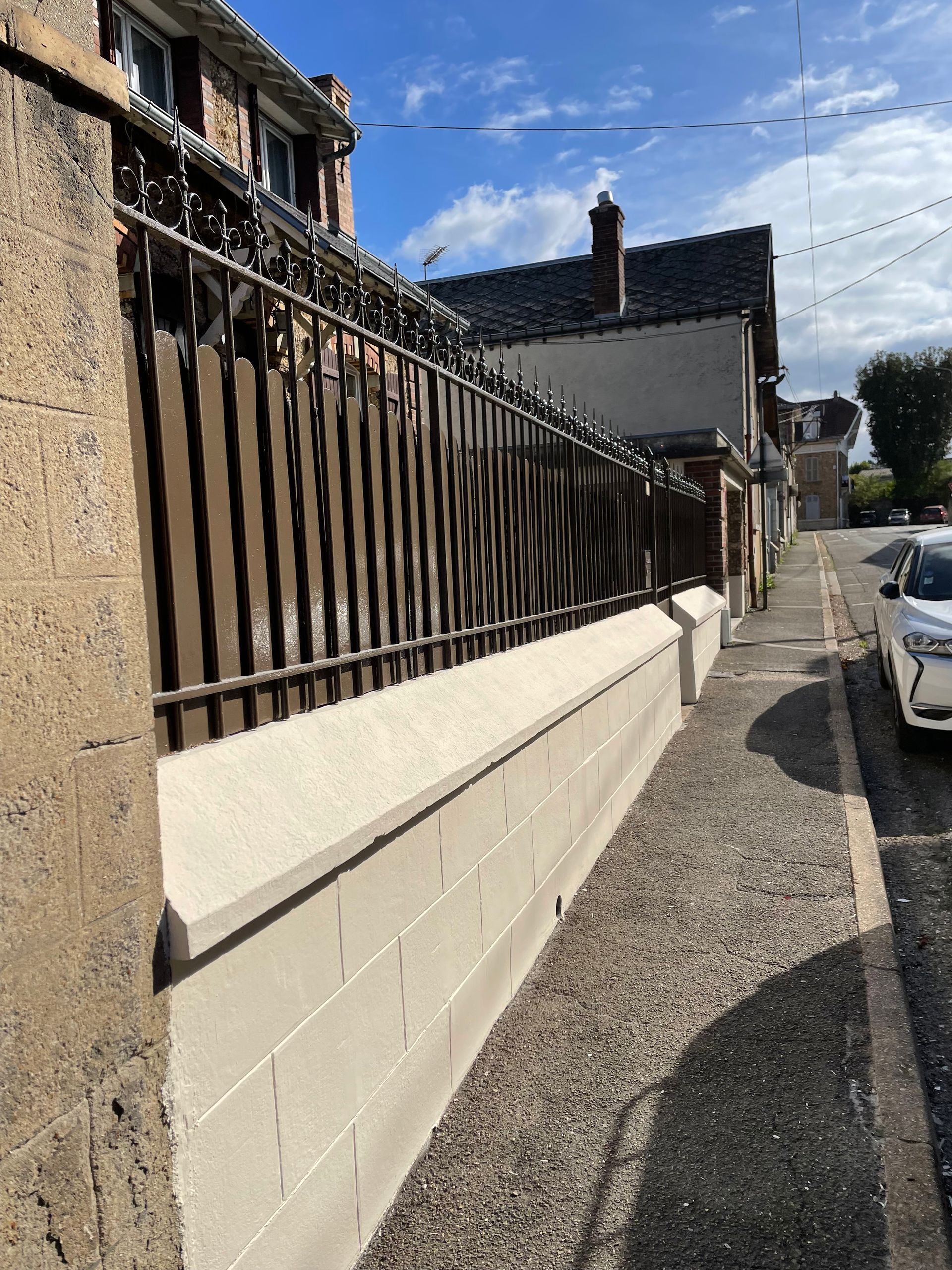 Mur en pierre avec une clôture métallique le long d'un trottoir devant un bâtiment.