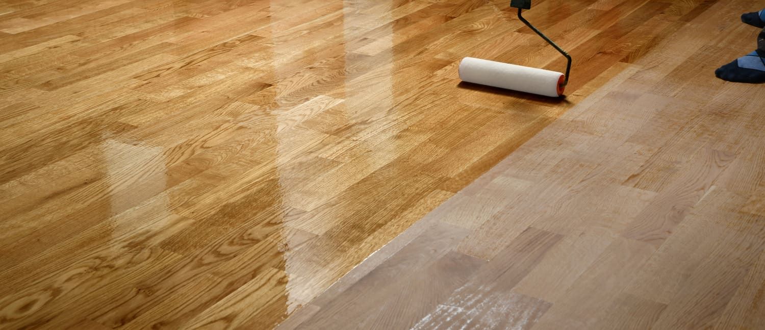 Una persona está pintando un piso de madera con un rodillo.