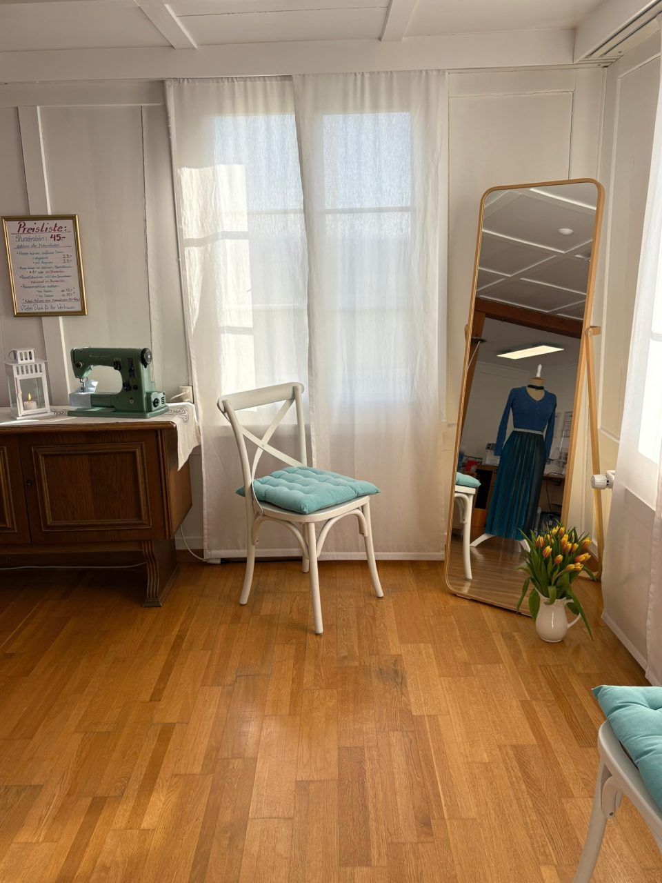 Ein Raum mit Hartholzböden, einem Stuhl, einem Spiegel und einer Nähmaschine.