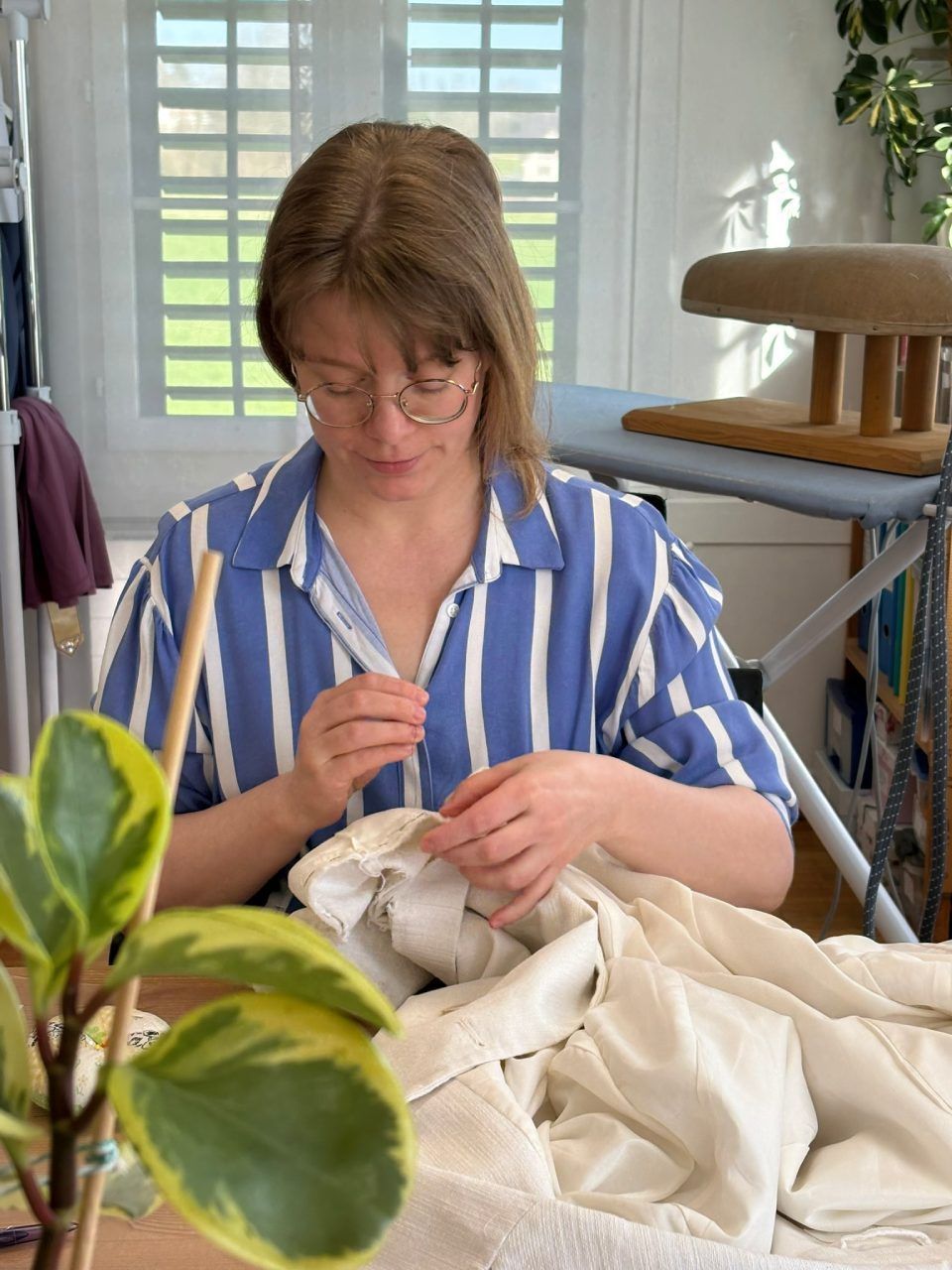 Eine Frau in einem blau-weiss gestreiften Hemd näht ein Stück Stoff.