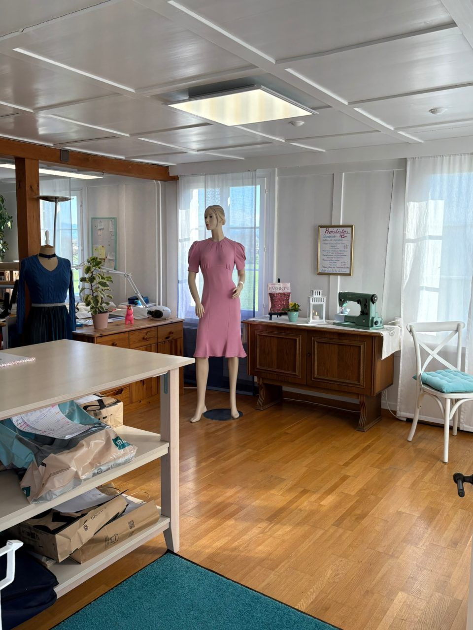 Eine Schaufensterpuppe in einem rosa Kleid steht in einem Raum mit einer Nähmaschine.