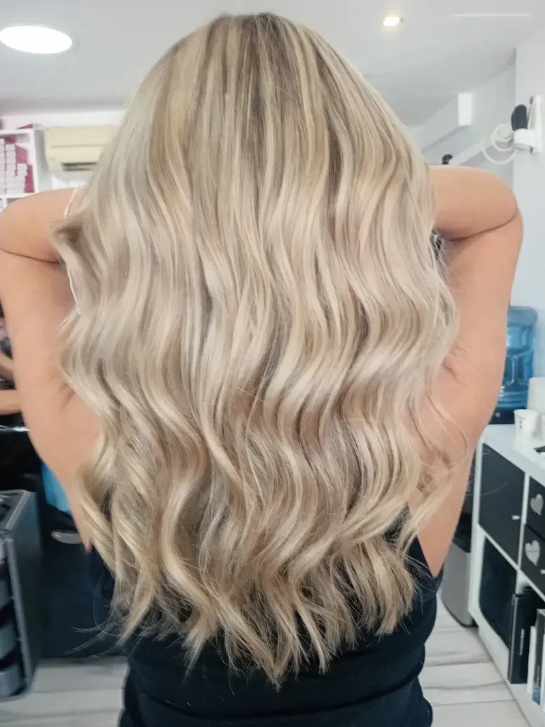 El cabello rubio con reflejos cae en cascada por la espalda de una persona, peinado en ondas sueltas.