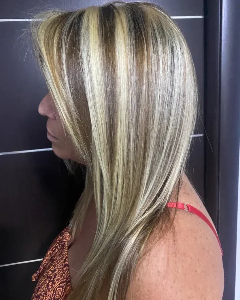 Mujer con reflejos rubios y castaños, vestida con una camiseta roja sin mangas, de pie junto a una pared oscura.