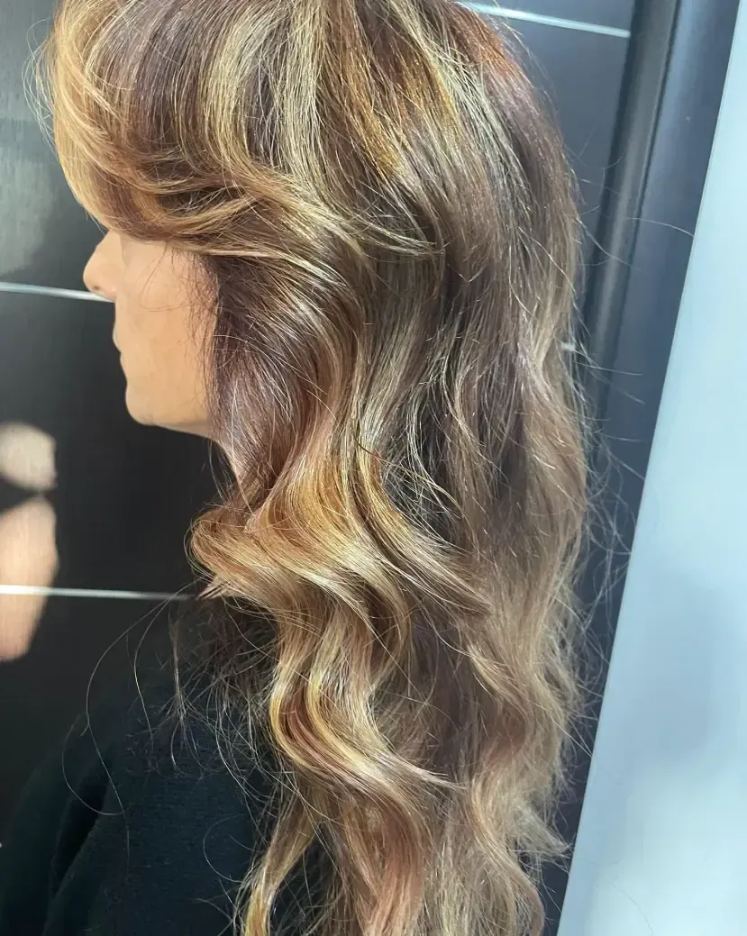 Mujer con cabello largo y ondulado, con reflejos rubios y castaños. Perfil lateral.