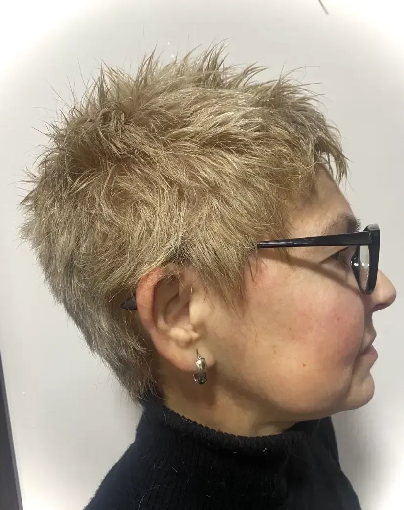 Persona con cabello rubio corto y puntiagudo, con gafas negras y cuello alto negro. Vista de perfil.