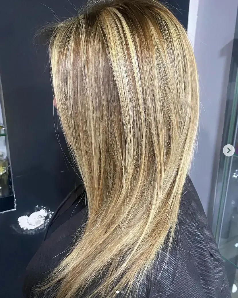 Mujer con reflejos rubios y castaños, cabello largo, peinado con capas texturizadas.