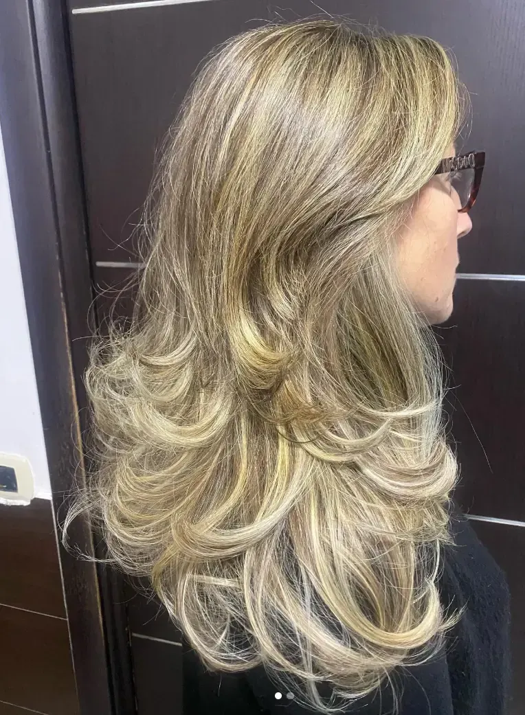 Mujer con cabello rubio largo en capas, perfil lateral.