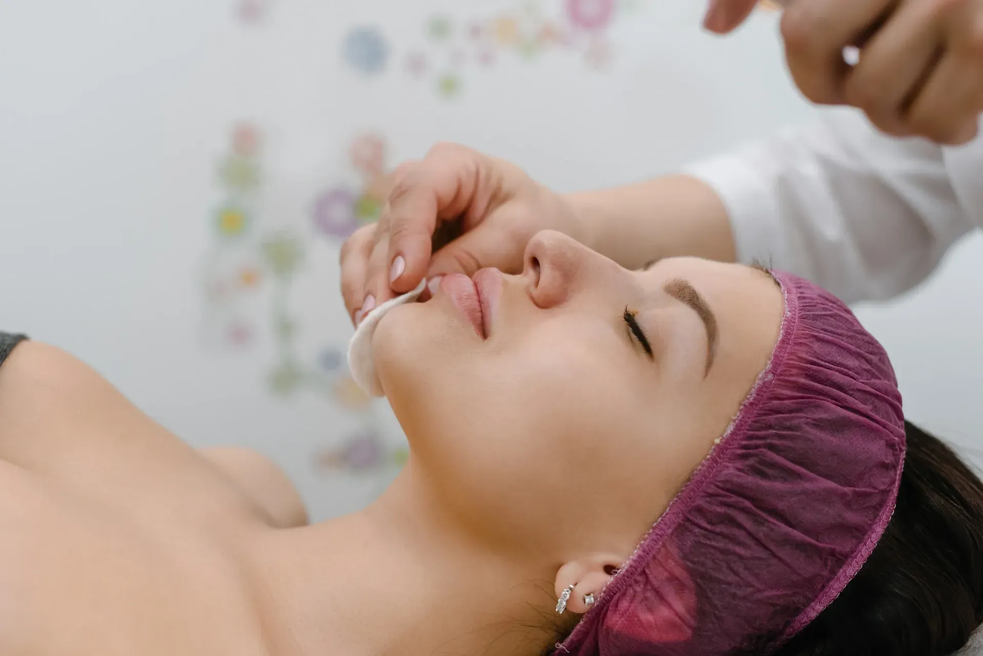 Mujer recibiendo un tratamiento facial, con los ojos cerrados, acostada en una mesa en un entorno de spa.