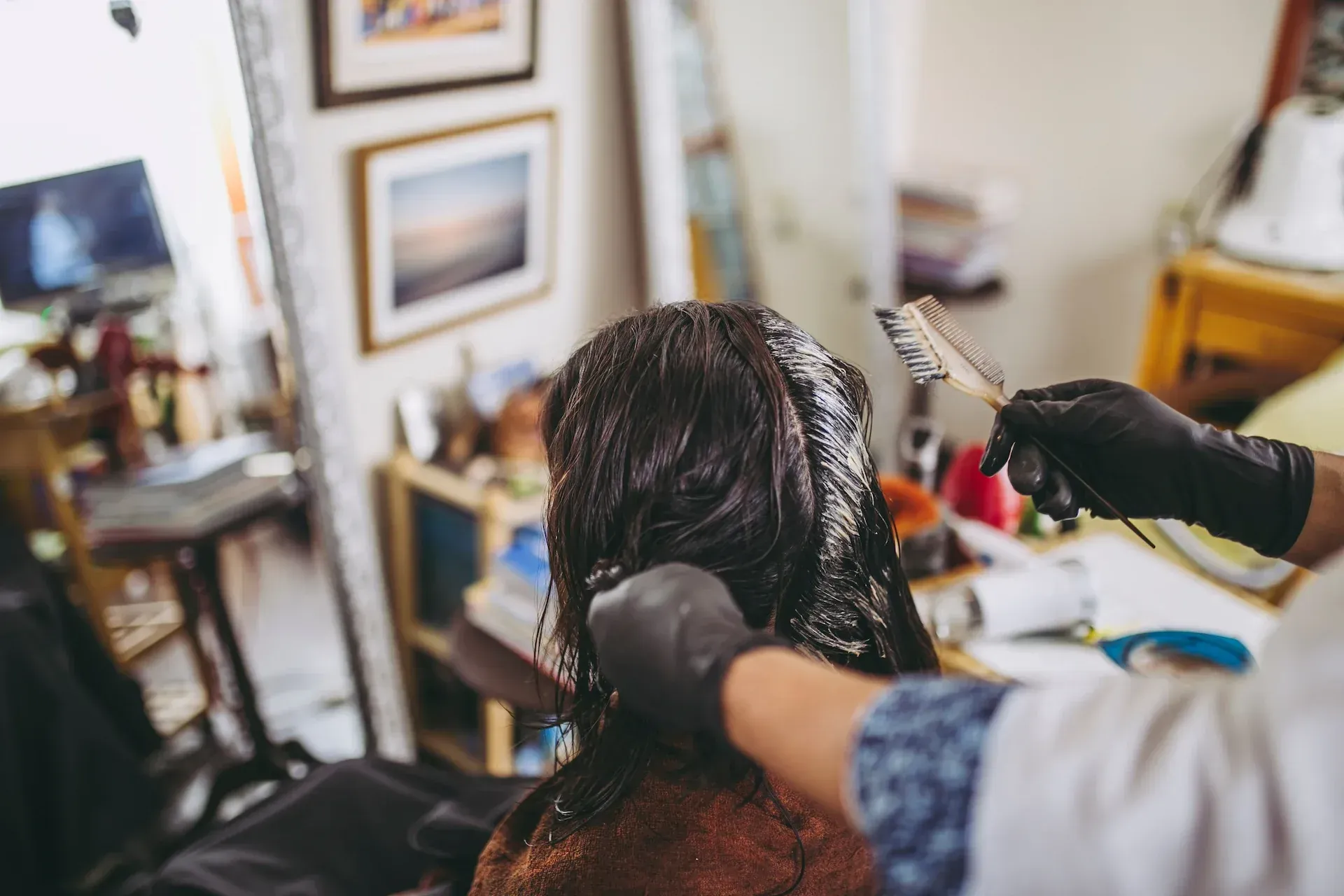 Persona que se tiñe el cabello en un salón; las manos enguantadas del estilista aplican el tinte con un cepillo.
