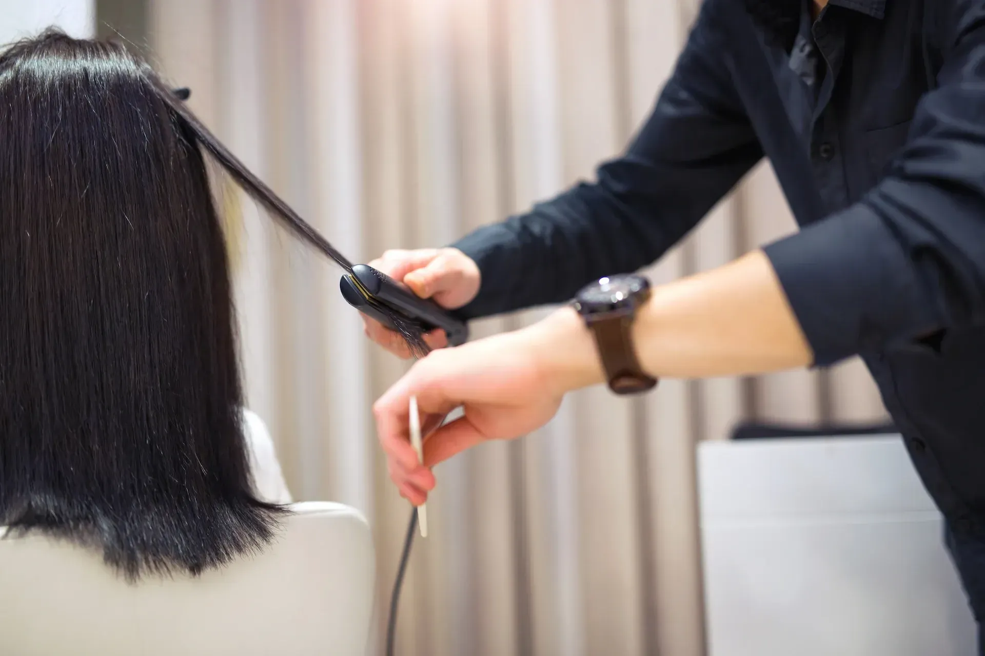 Peluquera alisando cabello oscuro con una plancha en un salón.