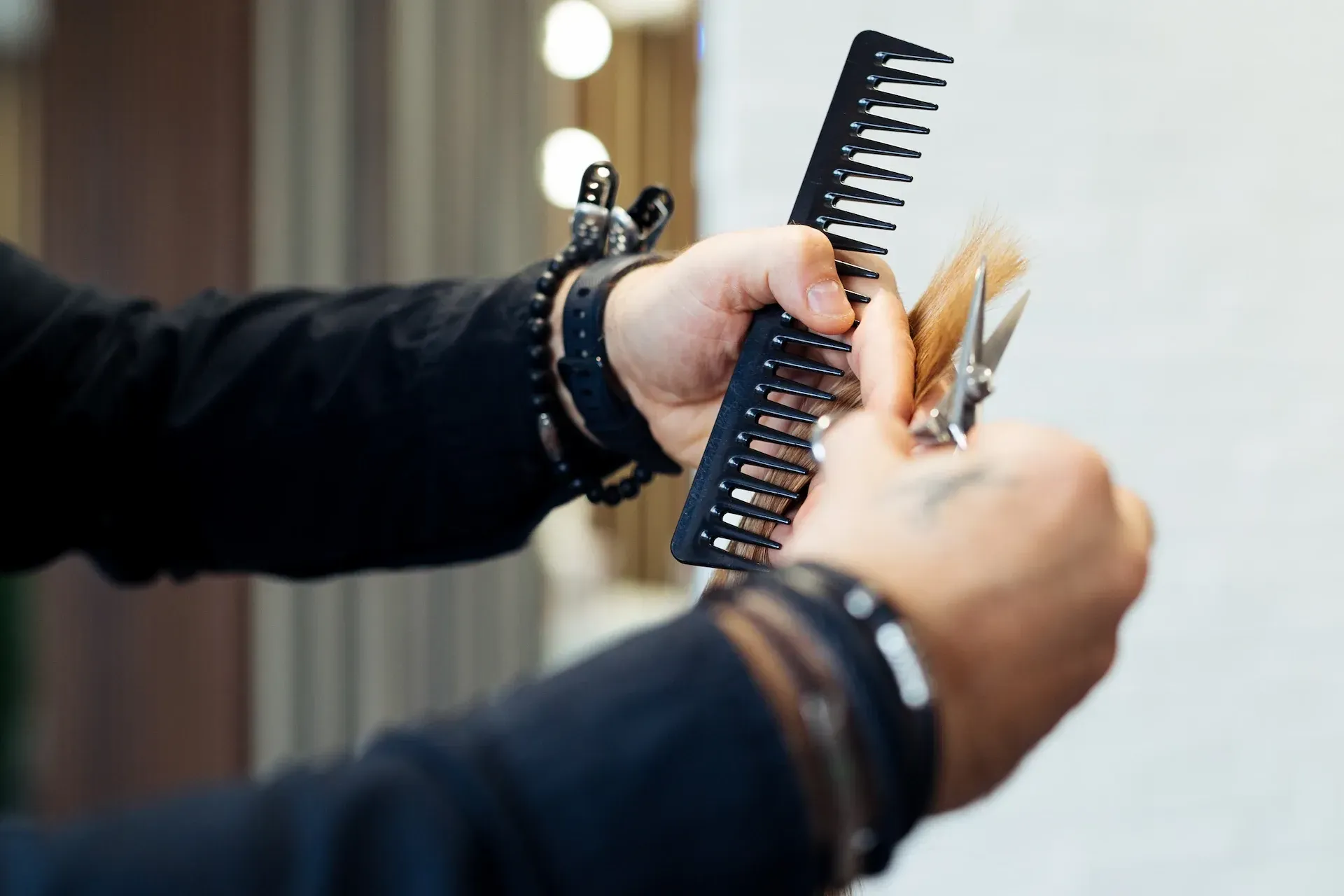 Manos del peluquero utilizando un peine para sujetar la sección de cabello, cortándolo con tijeras.