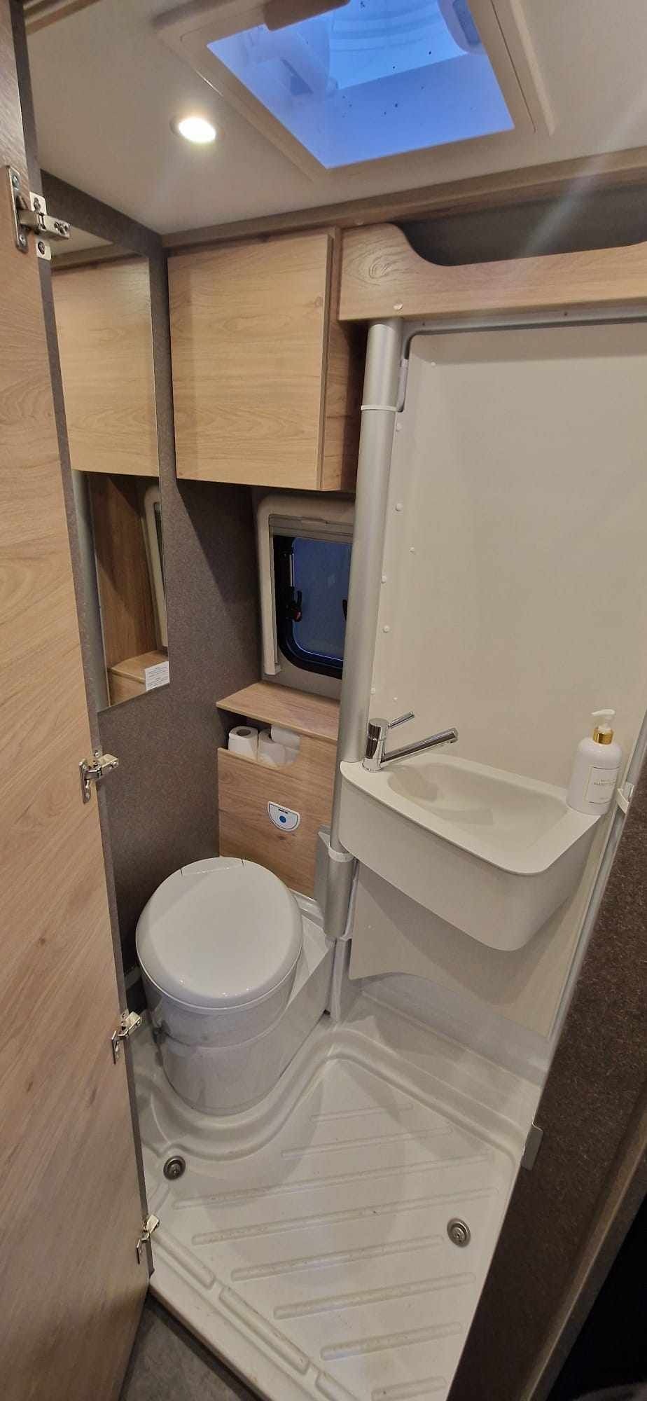Un pequeño baño para RV con inodoro, lavabo, ducha y armarios de almacenamiento.