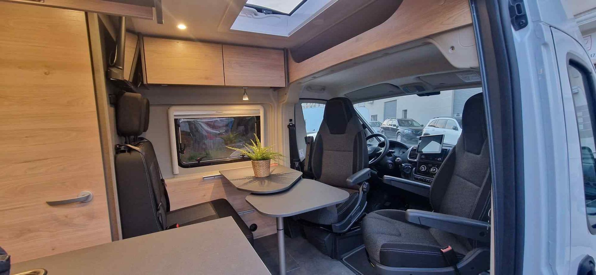 Interior de una autocaravana: zona de asientos con mesa, ventana, armarios superiores y asiento del conductor.