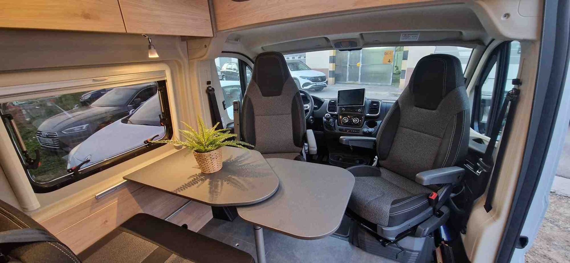 Interior de una furgoneta camper con mesa, asientos y vista a través del parabrisas.