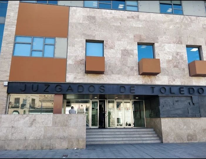 Exterior del edificio de los Juzgados de Toledo, con escaleras de acceso a la entrada, fachada de piedra y detalles en marrón.