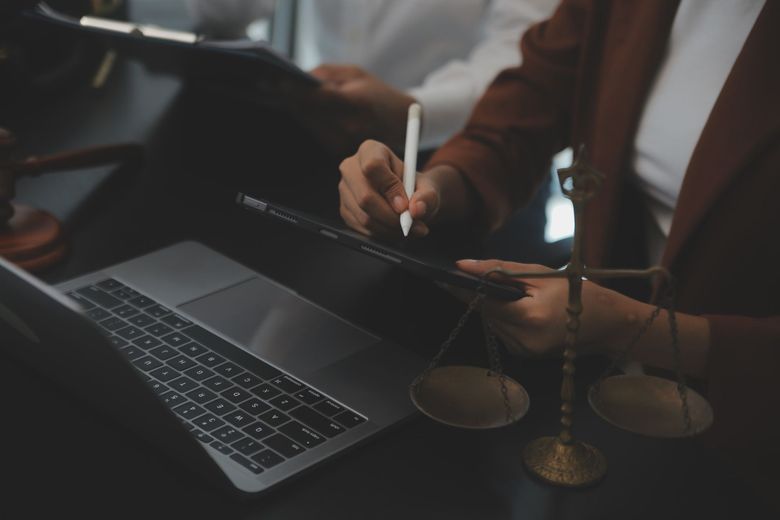 Personas que usan tabletas y computadoras portátiles con balanzas de justicia sobre el escritorio.