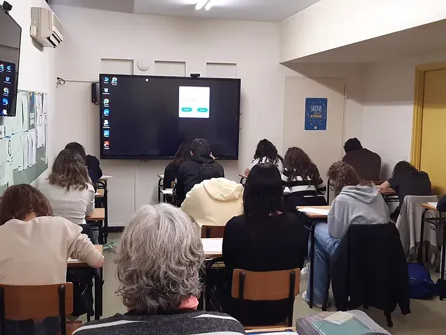 Un grupo de personas está sentada frente a una pantalla grande en un aula.