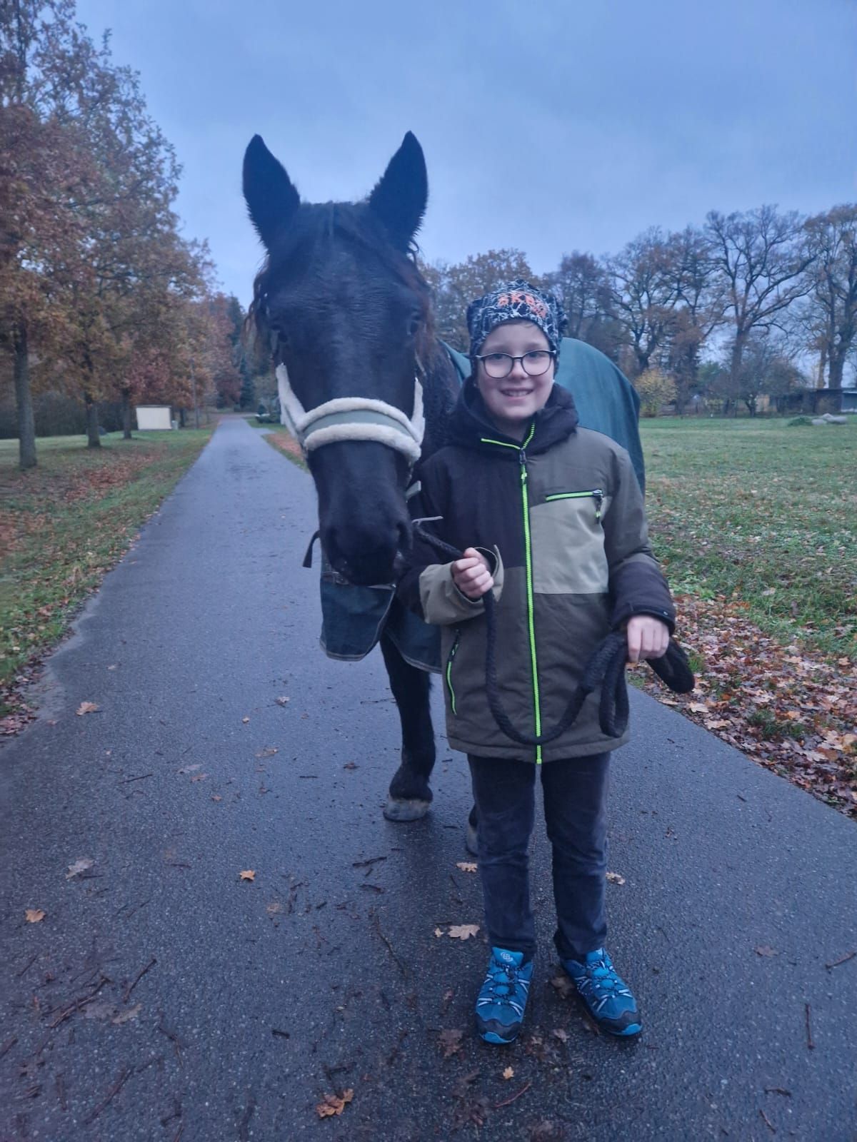 Ein kleiner Junge steht neben einem schwarzen Pferd auf einem Weg.