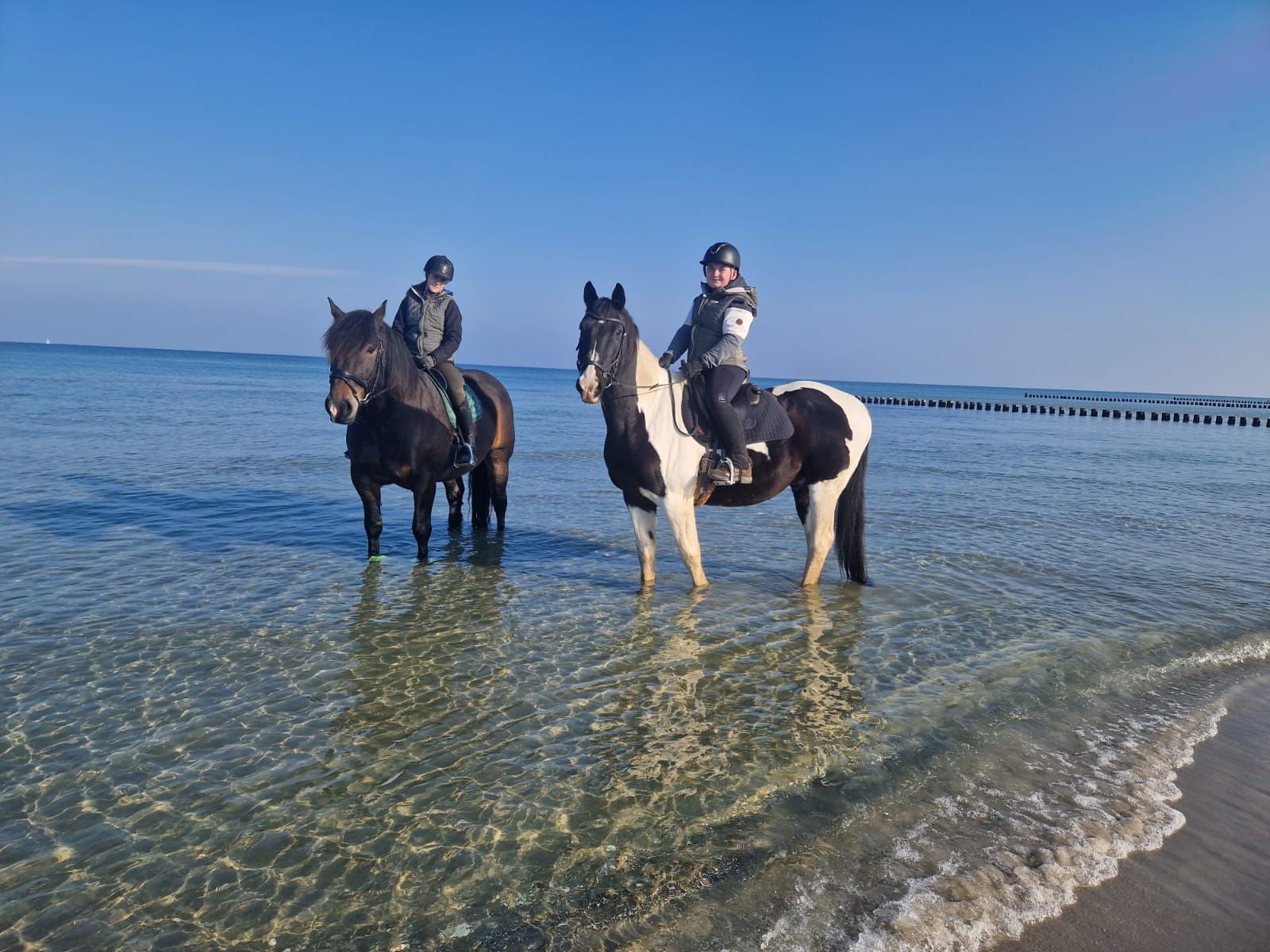 Zwei Personen reiten am Strand.