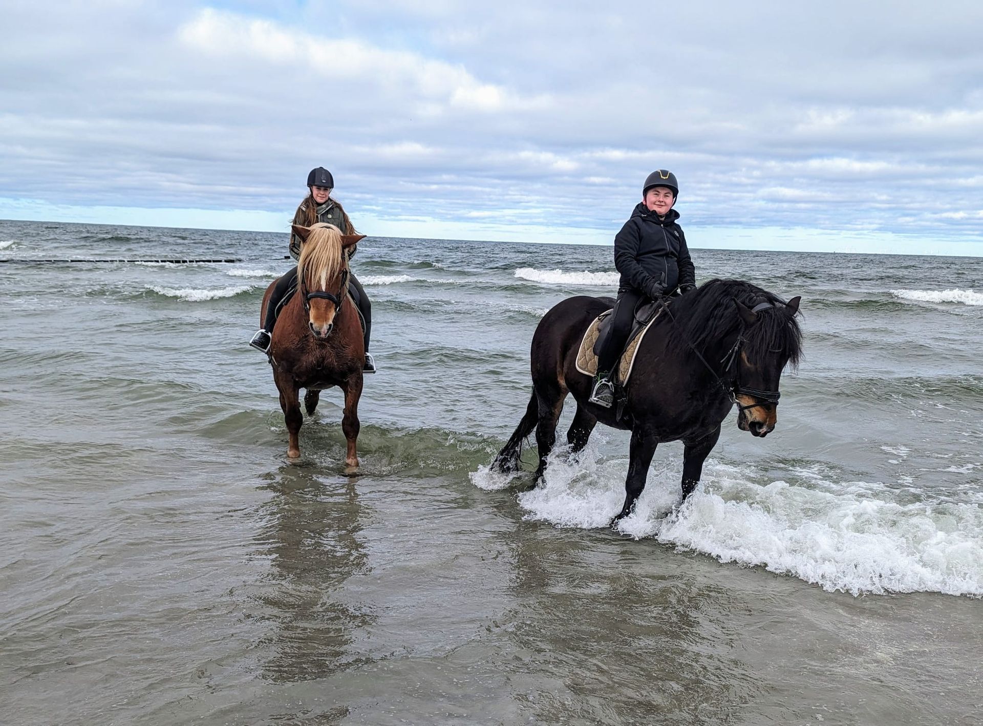 Zwei Personen reiten am Strand.