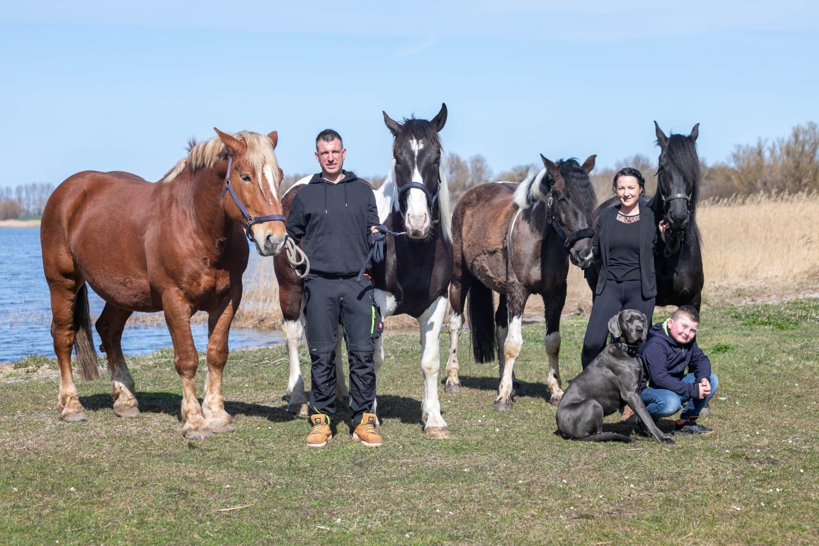 Eine Gruppe von Menschen steht neben Pferden und einem Hund auf einem Feld.