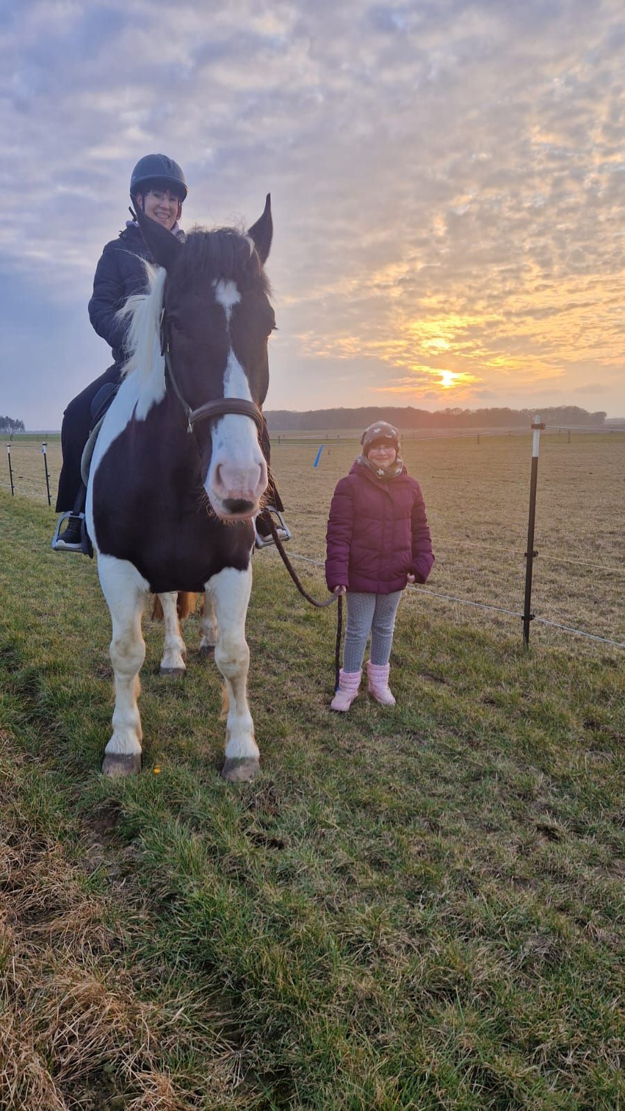 Eine Frau reitet auf einer Weide neben einem kleinen Mädchen.