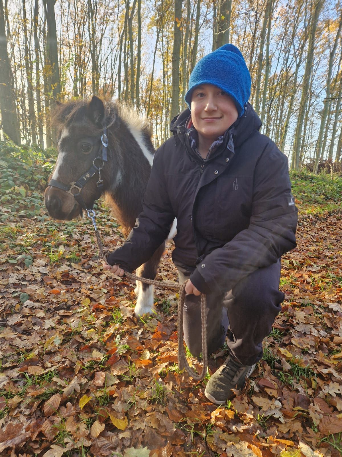 Eine Frau kniet neben einem kleinen Pferd im Wald.