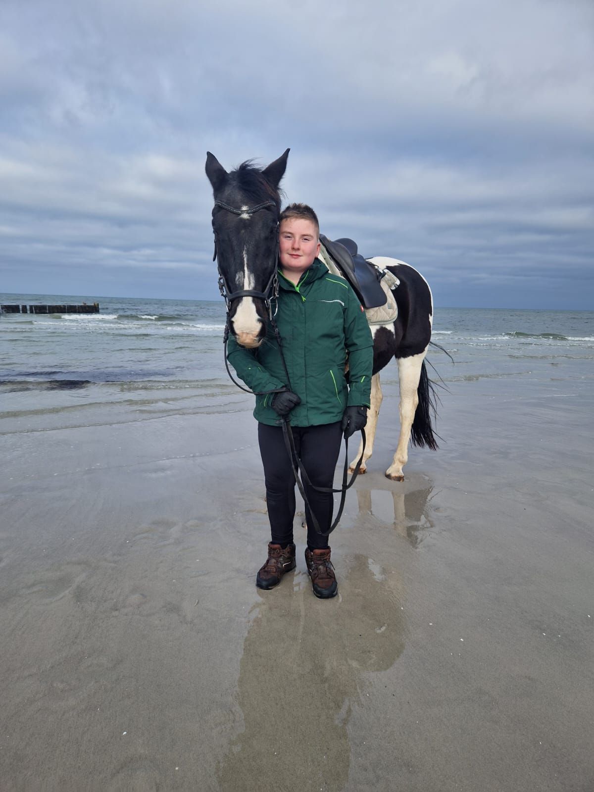 Eine Frau steht neben einem schwarz-weißen Pferd am Strand.