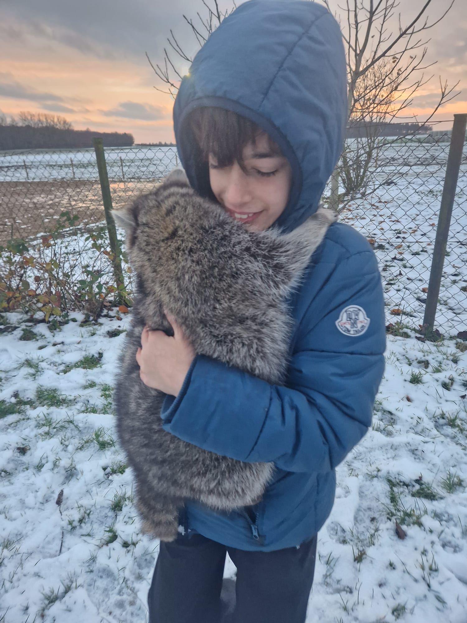 Ein kleiner Junge hält im Schnee eine Katze in seinen Armen.