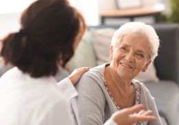 Eine ältere Frau sitzt auf einem Sofa und unterhält sich mit einer Krankenschwester.