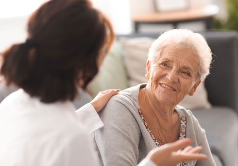 Eine ältere Frau sitzt auf einem Sofa und unterhält sich mit einer Krankenschwester.