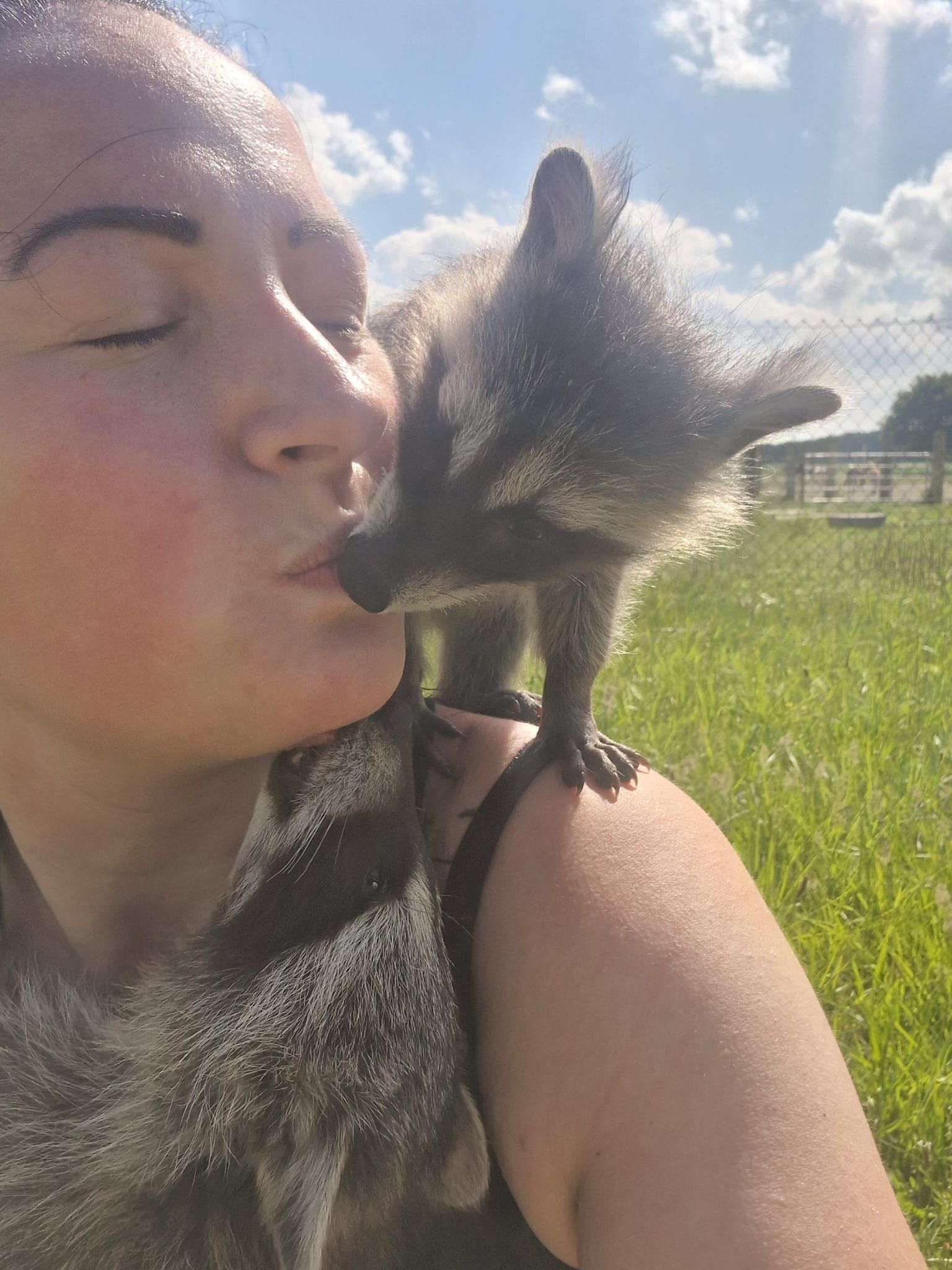 Eine Frau küsst einen kleinen Waschbären auf die Wange.
