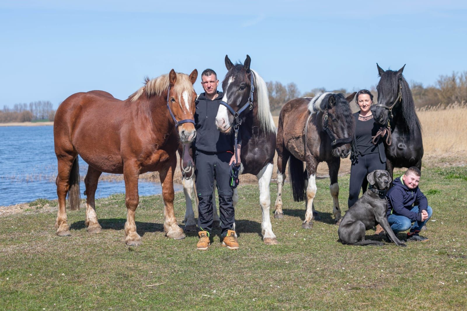 Eine Gruppe von Menschen steht neben Pferden und einem Hund auf einem Feld.
