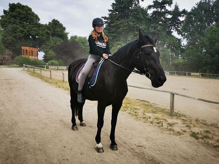 Eine Frau reitet auf einem schwarzen Pferd auf einem Feldweg