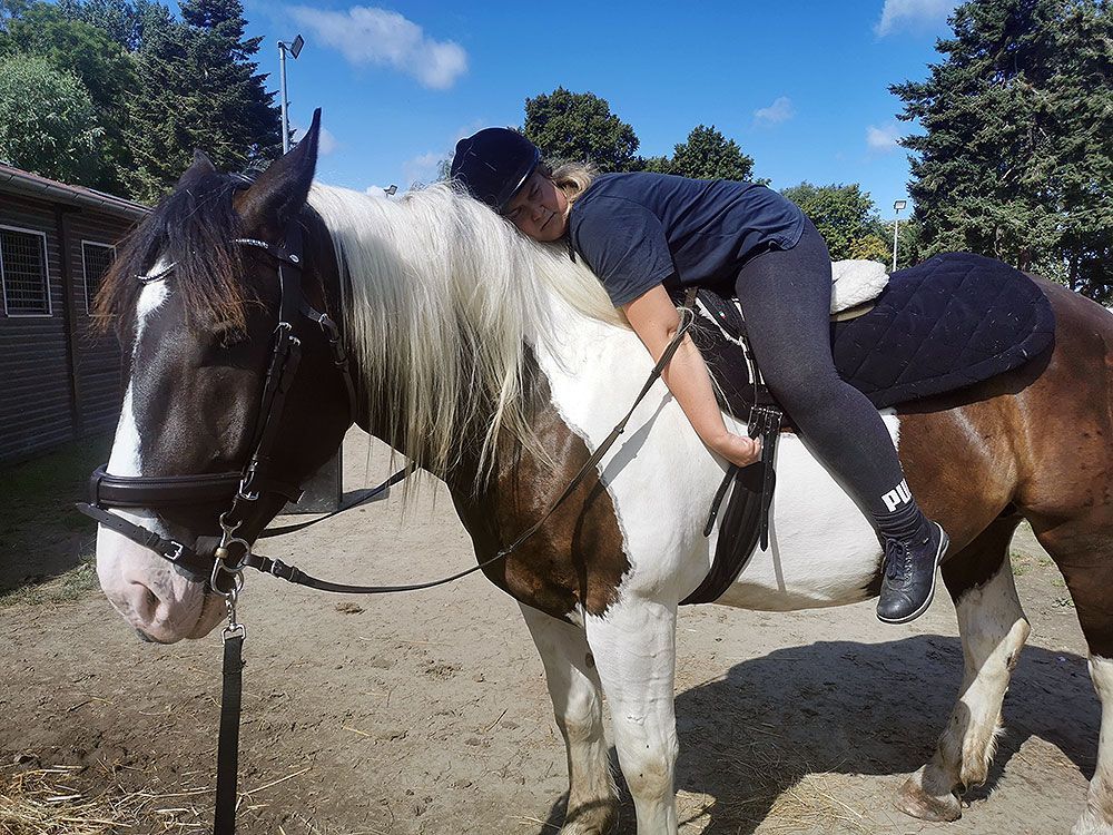 Eine Frau liegt auf dem Rücken eines braun-weißen Pferdes