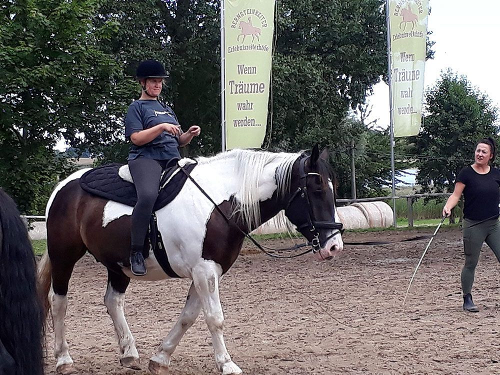 Eine Frau reitet auf einem braun-weißen Pferd über ein Feld.