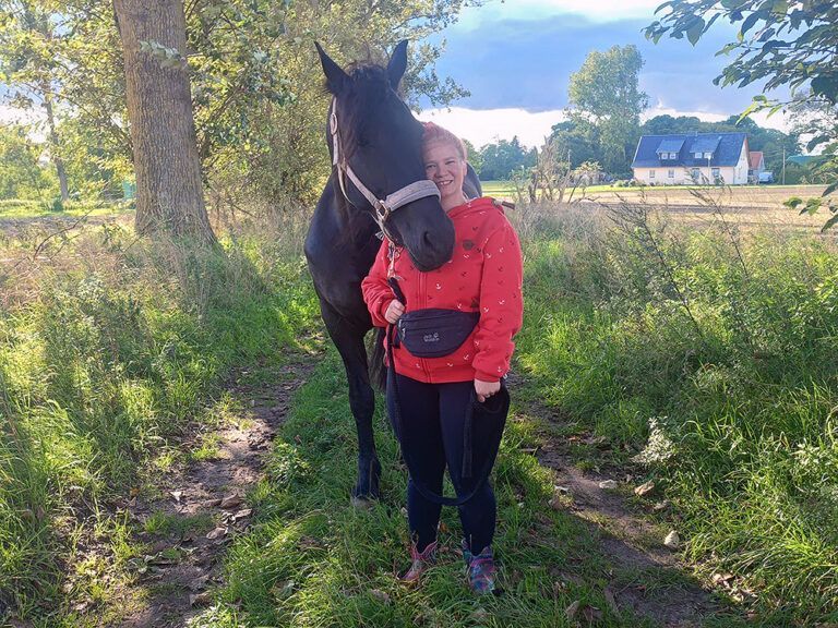 Eine Frau steht neben einem schwarzen Pferd auf einer Weide.