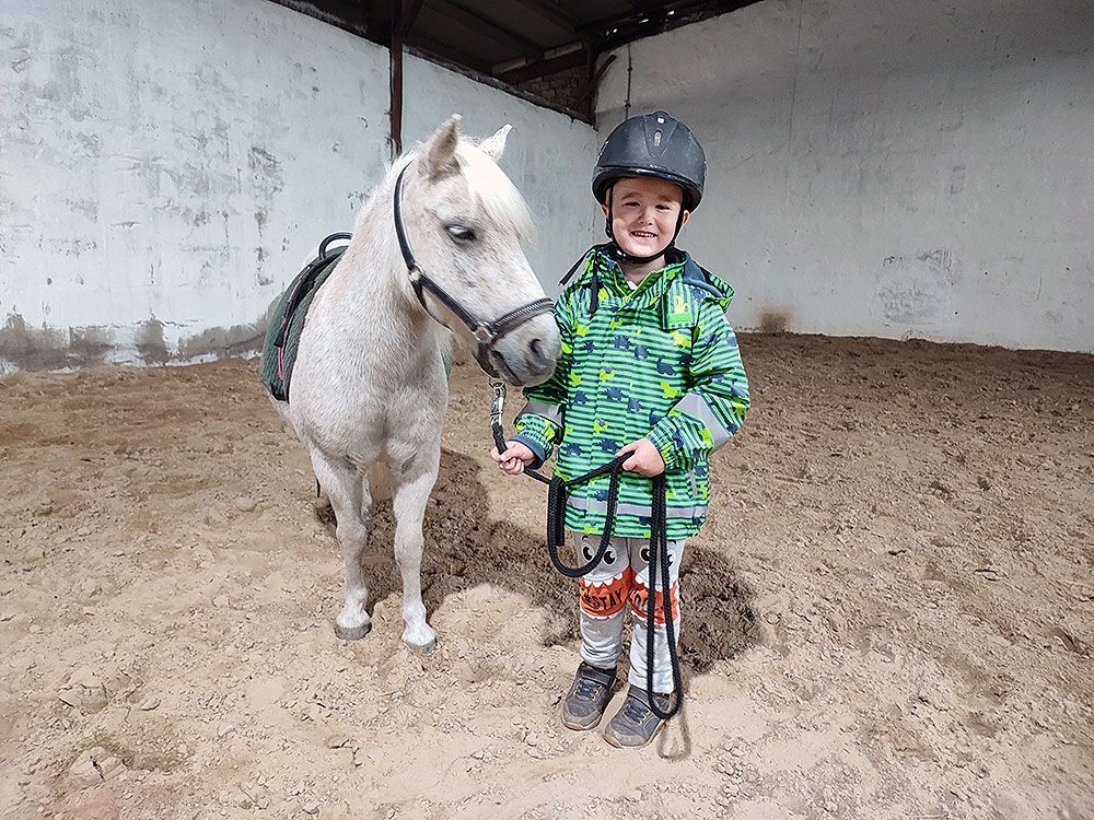 Ein kleiner Junge steht neben einem Pony in einem Stall.