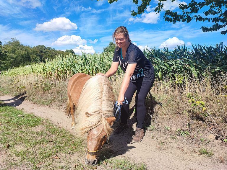 Eine Frau steht neben einem Pony auf einer Weide.