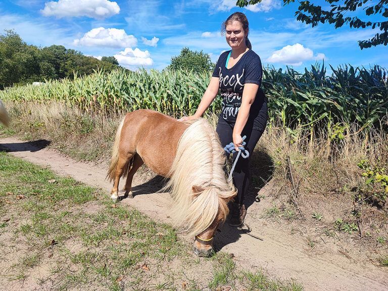 Eine Frau steht neben einem kleinen Pony auf einer Weide.