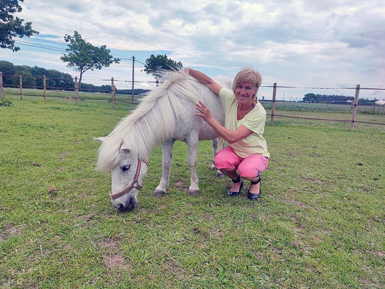 Eine Frau kniet neben einem weißen Pony auf einem Feld