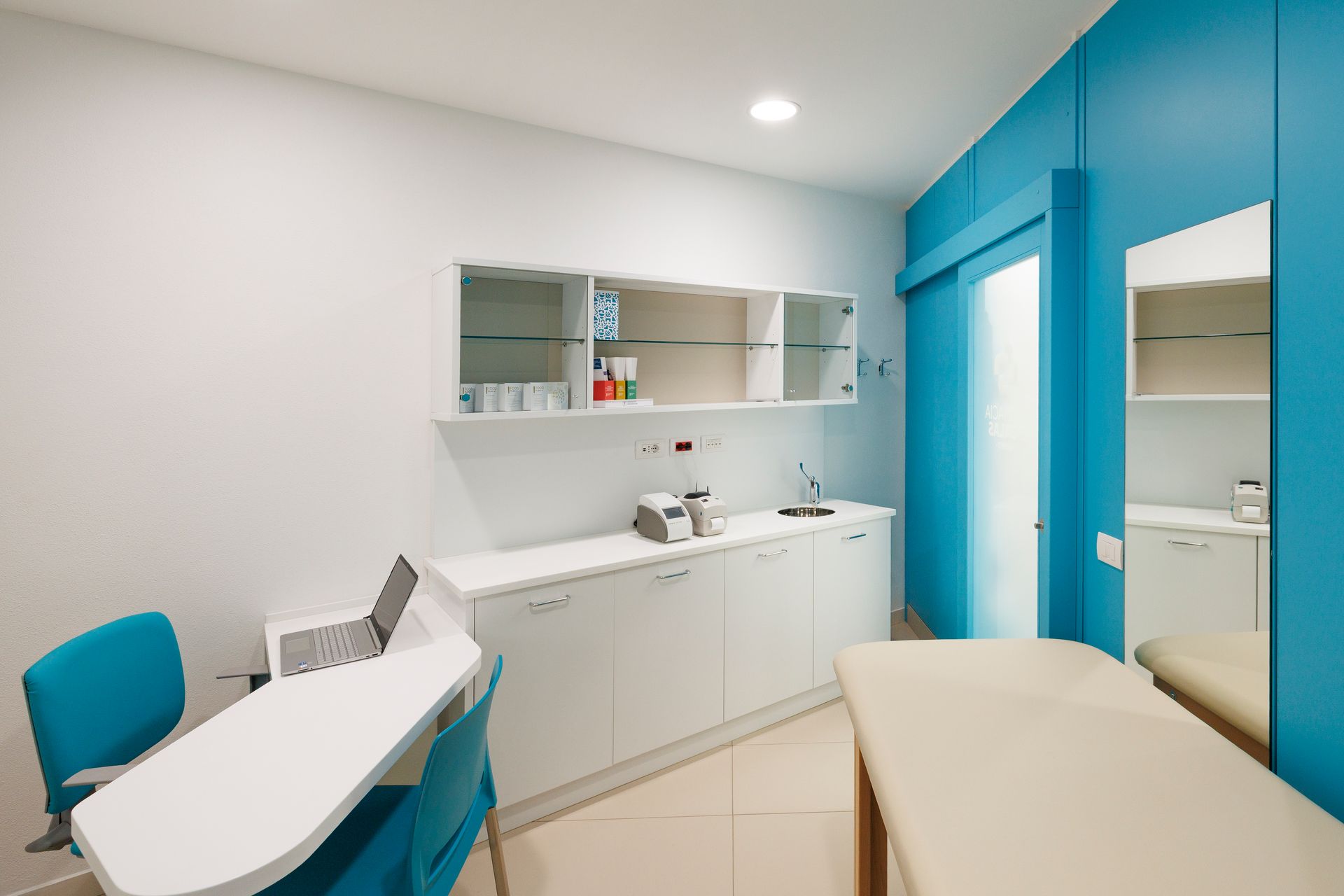Sala visite odontoiatriche con mobili bianchi, pareti blu e poltrona reclinabile.