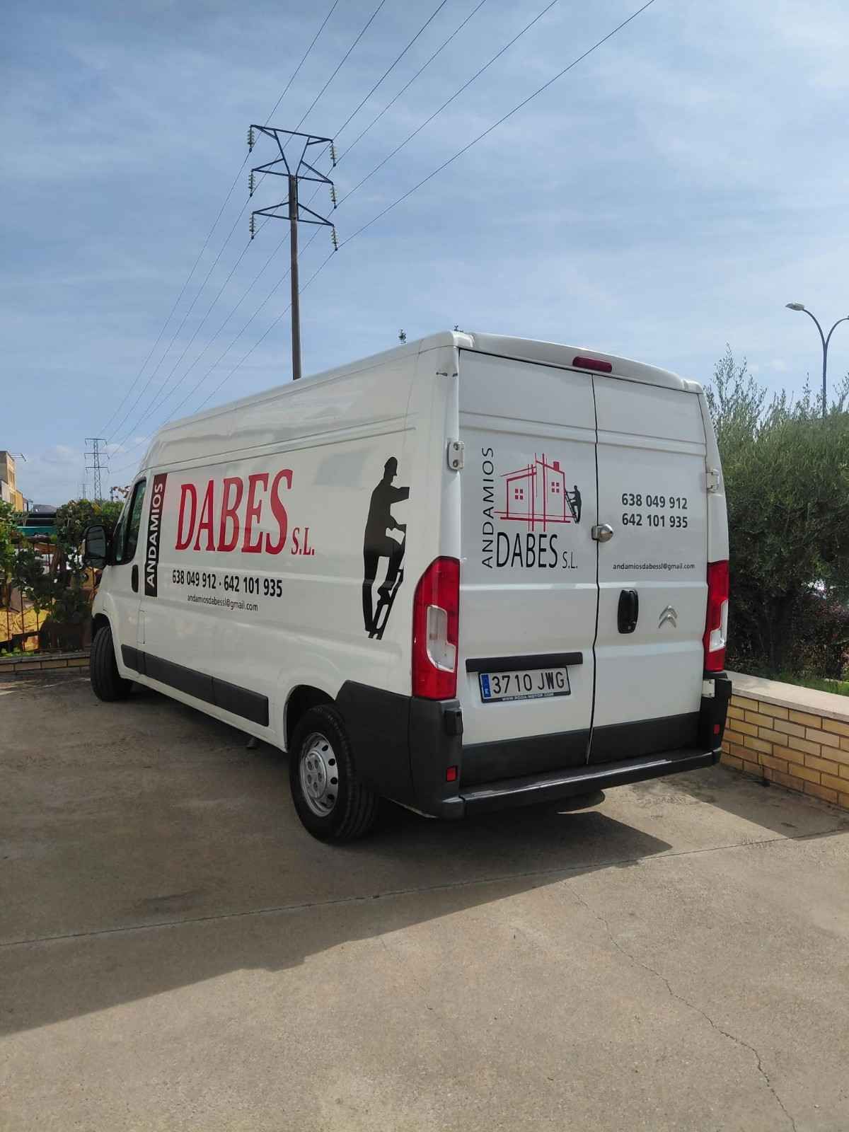 Furgoneta blanca de reparto con el logotipo «DABES» aparcada junto a la carretera bajo un cielo azul.