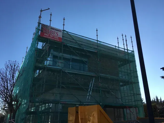Edificio en construcción con andamios cubiertos por una malla verde, bajo un cielo azul