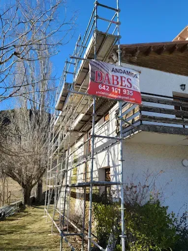 Andamios junto a una casa blanca, con un cartel rojo y blanco bajo un cielo azul