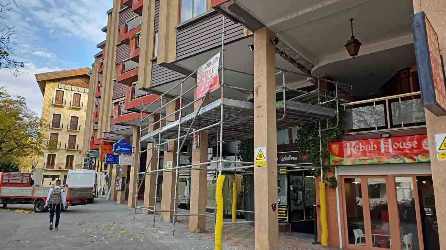 Calle con furgonetas aparcadas, un ciclista y tiendas bajo una galería cubierta.