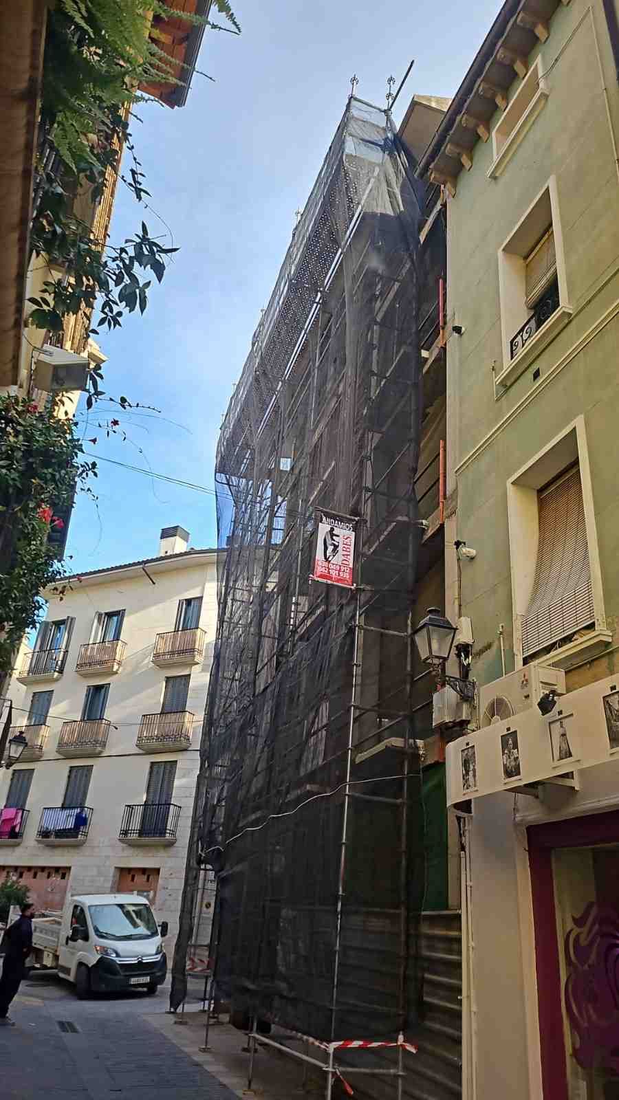 Calle estrecha de la ciudad con un edificio alto cubierto de una malla negra para andamios, junto a edificios de apartamentos