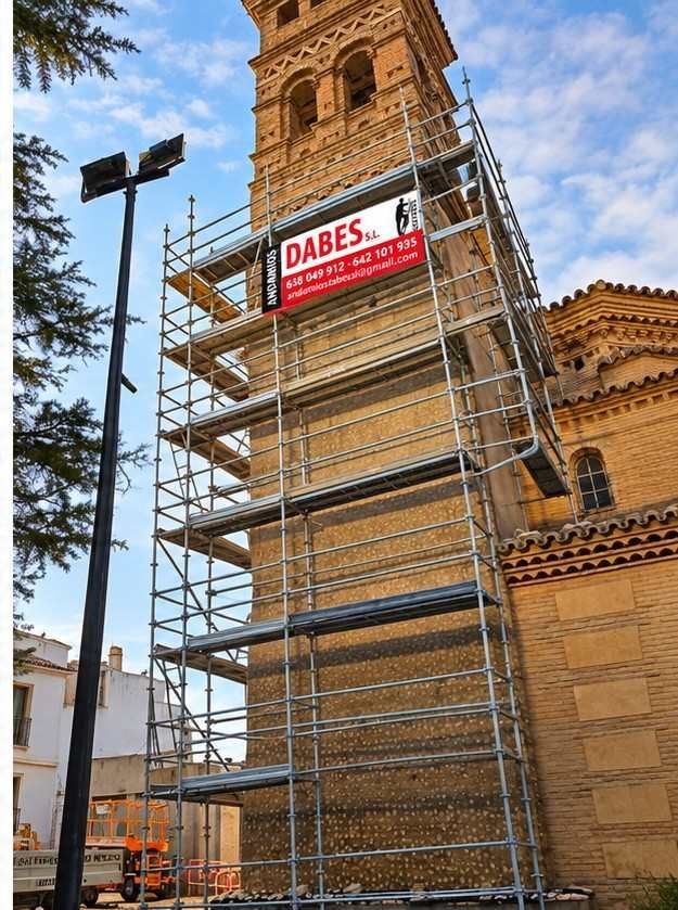 Torre histórica rodeada de andamios, con un letrero rojo de DABES y trabajadores en una escena urbana callejera