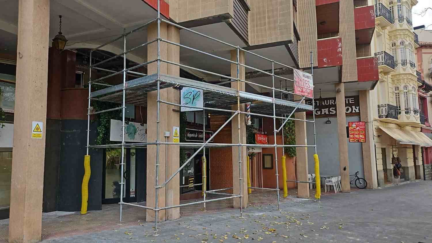 Fachada de un edificio a pie de calle, con andamios, escaparates de cristal y una tranquila acera urbana